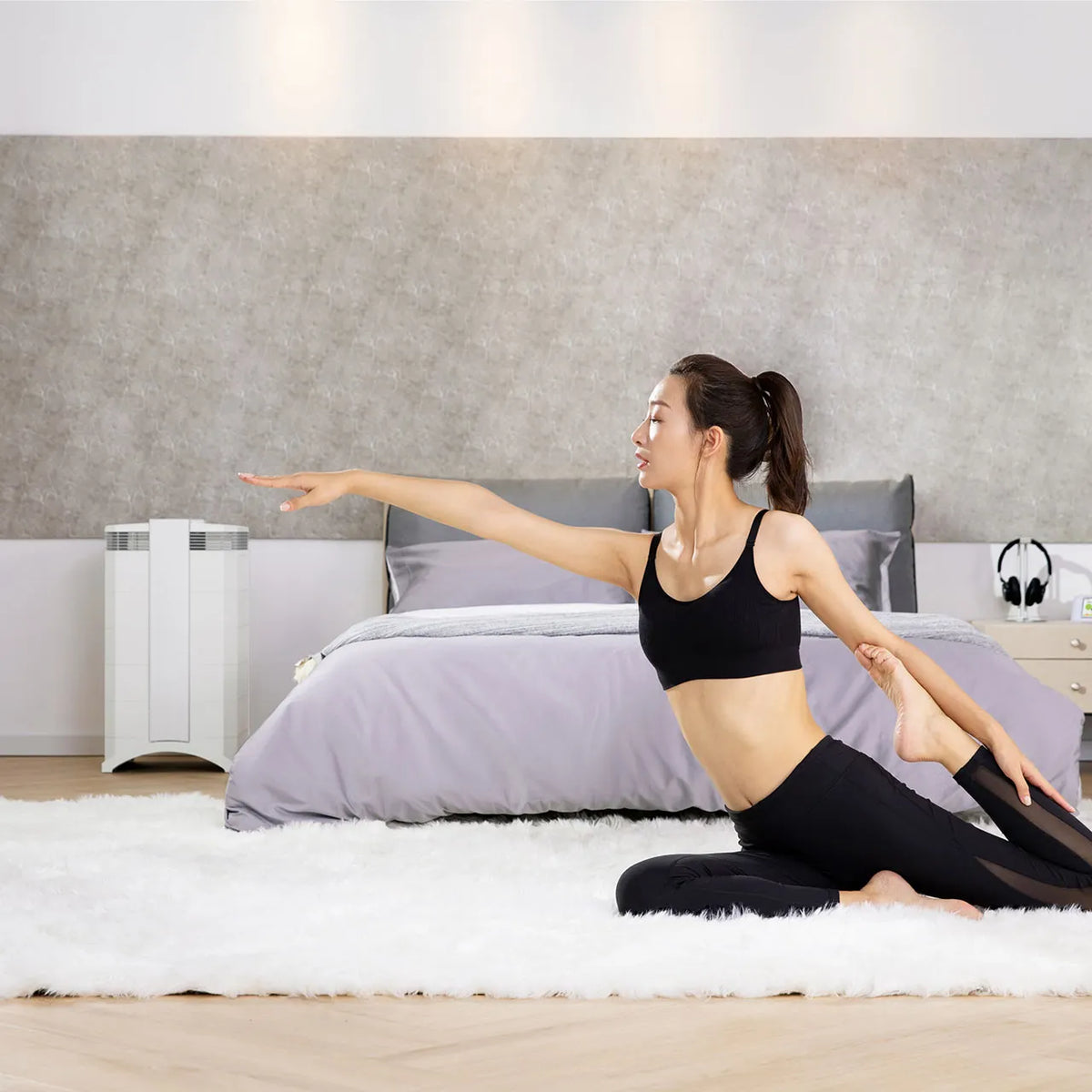 Frau macht Yoga-Übung im Schlafzimmer, im Hintergrund weißer IQAir HealthPro 250 XE Luftreiniger neben dem Bett
