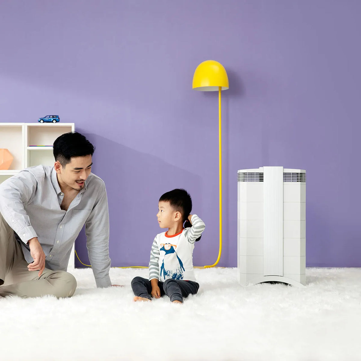Vater und Kind sitzen auf Teppich im Kinderzimmer neben weißem IQAir HealthPro 250 XE Luftreiniger