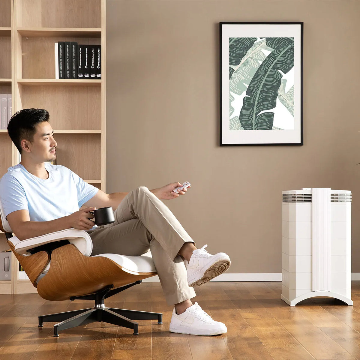 Mann sitzt im Lounge-Sessel mit Fernbedienung neben weißem IQAir HealthPro 250 XE Luftreiniger im Wohnzimmer