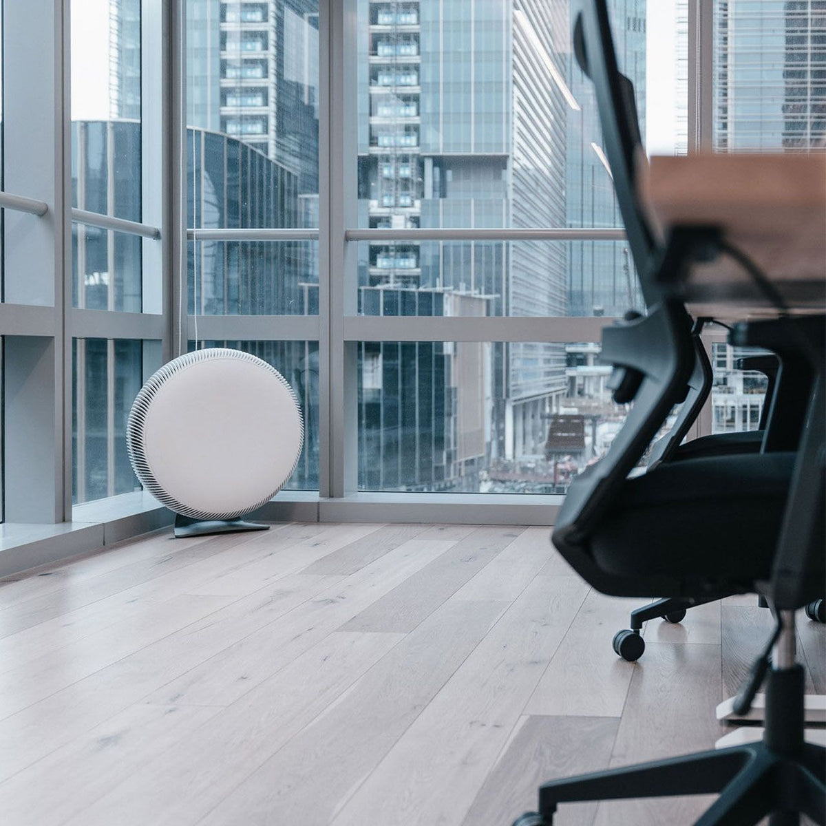 IQAir Atem X Luftreiniger, rund und weiß, im Büro vor Fensterfront mit Skyline-Blick