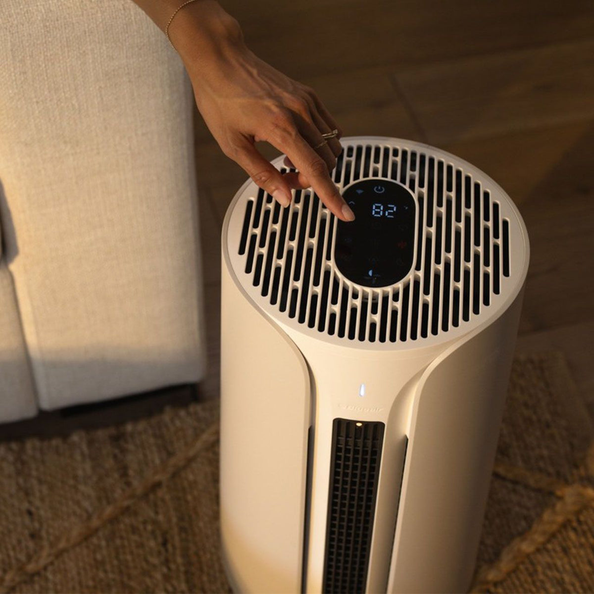 Hand bedient das Touch-Display des weißen Blueair ComfortPure T10i Luftreinigers im Wohnzimmer
