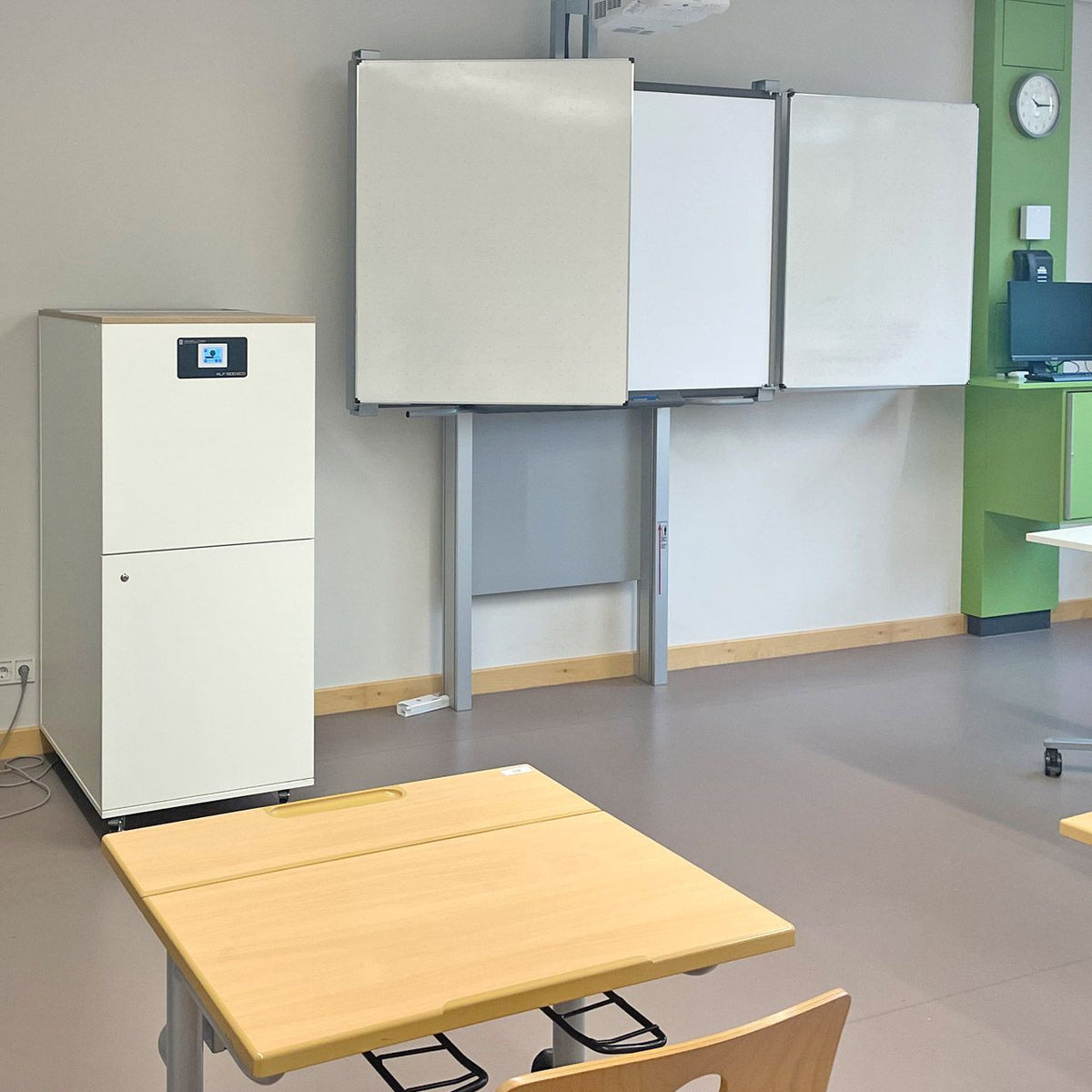 HS Solution RLF 1500 ECO Luftreiniger in einem Klassenzimmer neben Whiteboards und Schülertisch