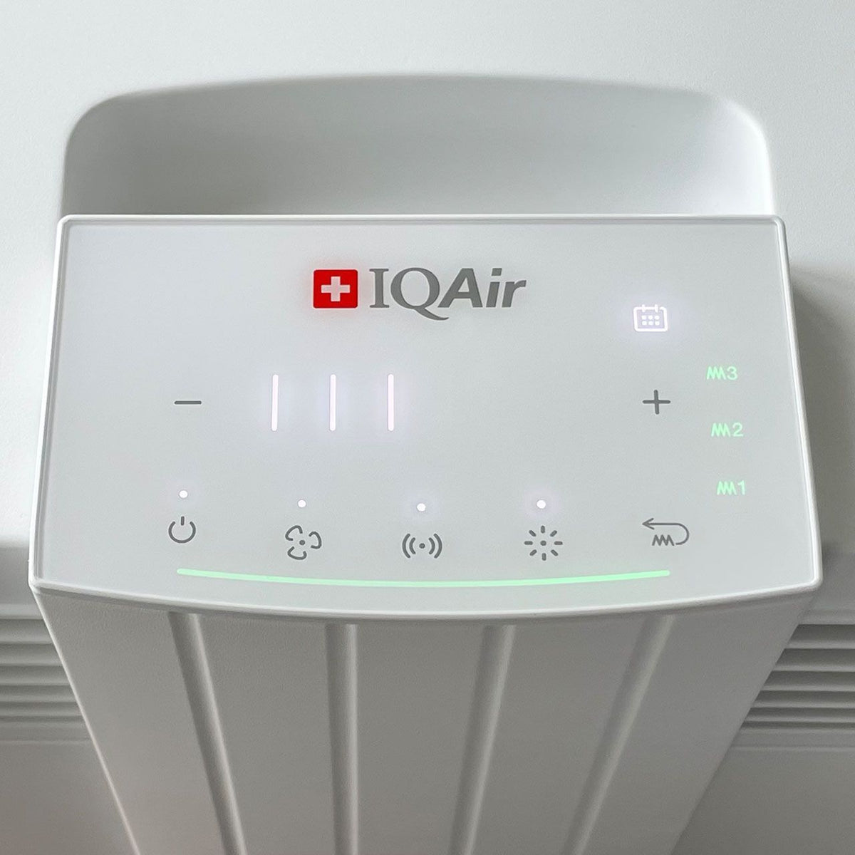 Nahaufnahme des Bedienfelds des IQAir HealthPro 100 XE Luftreinigers mit Touch-Symbolen und grünem Leuchtstreifen