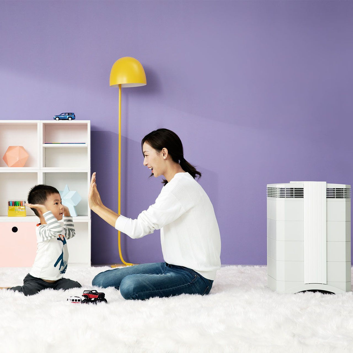 Mutter und Kind spielen im Kinderzimmer neben weißem IQAir HealthPro 100 XE Luftreiniger