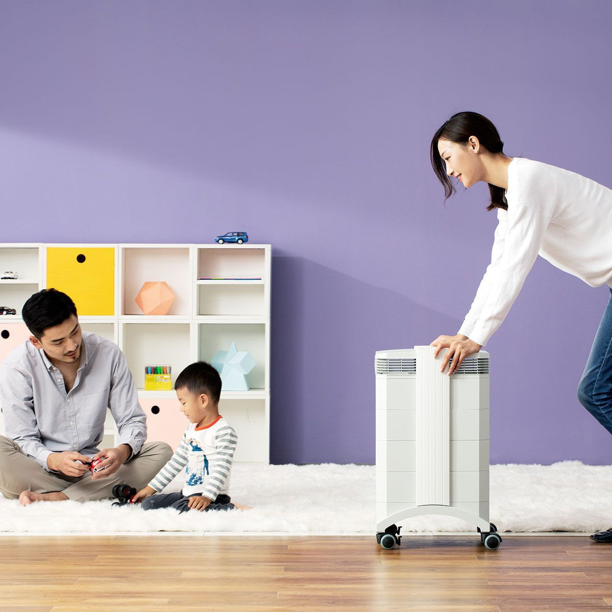 Frau bedient IQAir HealthPro 100 XE Luftreiniger im Kinderzimmer, Vater und Kind spielen auf Teppich