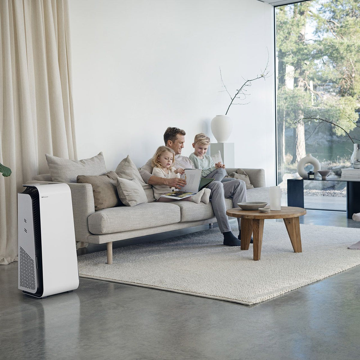 Blueair HealthProtect™ 7740i Luftreiniger steht im Wohnzimmer neben Sofa mit Vater und Kindern